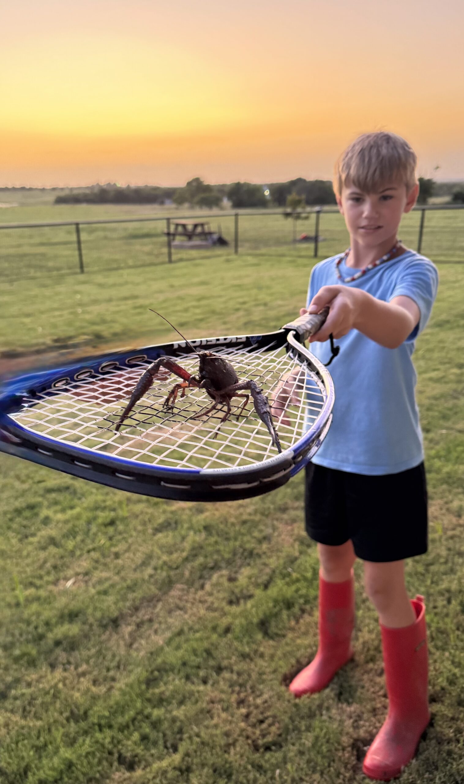 Camdyn holds January the crawdad at arm's length atop a tennis racket